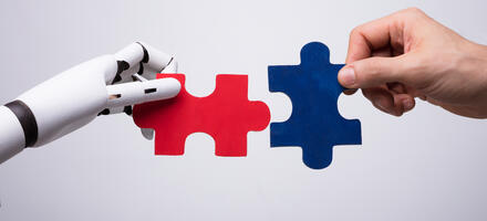 Robot hand and human hand holding puzzle pieces as a way of representing collaboration