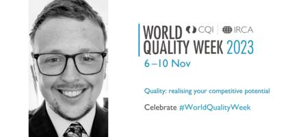 Mitchell Reed is pictured smiling in a suit and tie wearing glasses. The World Quality Week logo is to the right