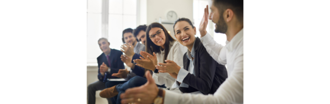 a diverse range of professionals are seated in a row in an office, smiling and clapping in a collaborative manner