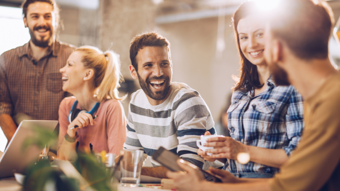 A group of five men and women smile in a sun-lit office. 