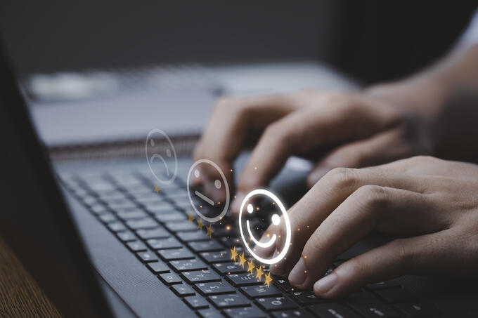 Laptop with hands typing and a graphic of a five star happy face rating
