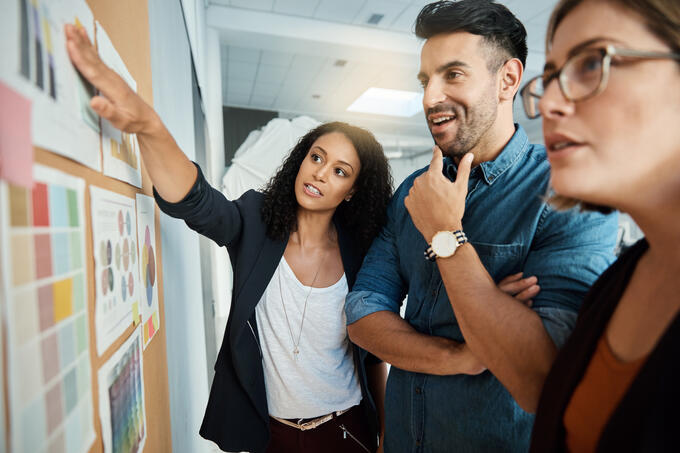 Three people standing up working together discussing concepts on a wall in an office