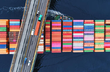 A tanker  of containers travels beneath a busy road bridge