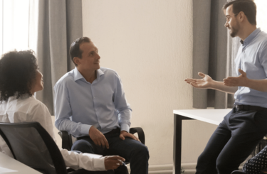 A diverse team of six gather in an office in conversation