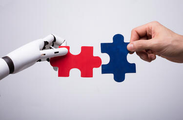 Robot hand and human hand holding puzzle pieces as a way of representing collaboration Robot hand and human hand holding puzzle pieces as a way of representing collaboration