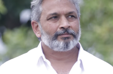 Murugesh Siva, a grey haired Indian man with beard and moustache in a white open necked shirt, outdoors