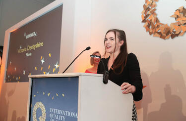 Victoria Derbyshire, young woman in black suit, speaking at the International Quality Awards 2022 event