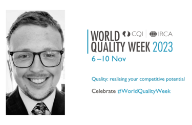 Mitchell Reed is pictured smiling in a suit and tie wearing glasses. The World Quality Week logo is to the right