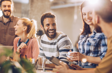 A group of five men and women smile in a sun-lit office.