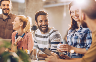 A group of five men and women smile in a sun-lit office. 