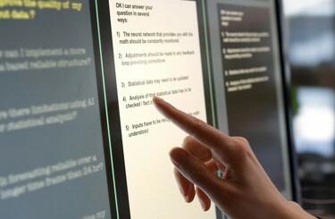 Large computer screen with finger pointing to text.