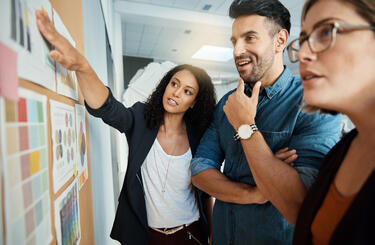 Three people standing up working together discussing concepts on a wall in an office