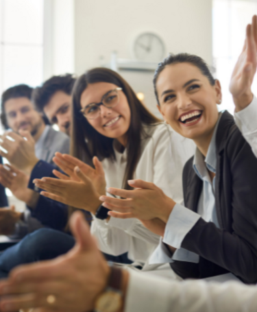 a diverse range of professionals are seated in a row in an office, smiling and clapping in a collaborative manner