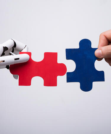 Robot hand and human hand holding puzzle pieces as a way of representing collaboration