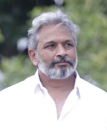 Murugesh Siva, a grey haired Indian man with beard and moustache in a white open necked shirt, outdoors