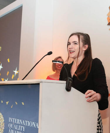 Victoria Derbyshire, young woman in black suit, speaking at the International Quality Awards 2022 event
