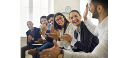 a diverse range of professionals are seated in a row in an office, smiling and clapping in a collaborative manner