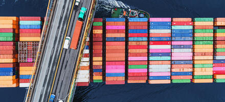 A tanker of containers travels beneath a busy road bridge