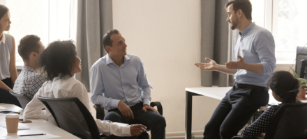 A diverse team of six gather in an office in conversation