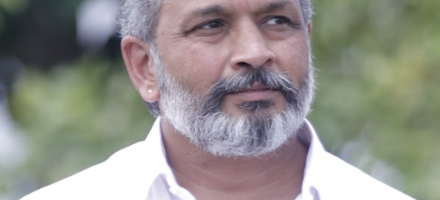 Murugesh Siva, a grey haired Indian man with beard and moustache in a white open necked shirt, outdoors