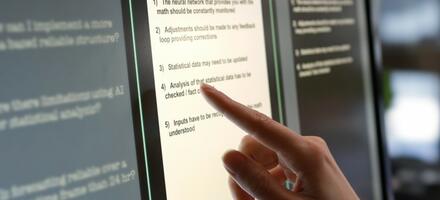 Large computer screen with finger pointing to text.