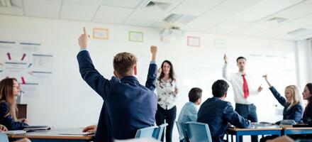 School pupils with their hands raised as teachers ask questions in a classroom