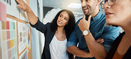 Three people standing up working together discussing concepts on a wall in an office