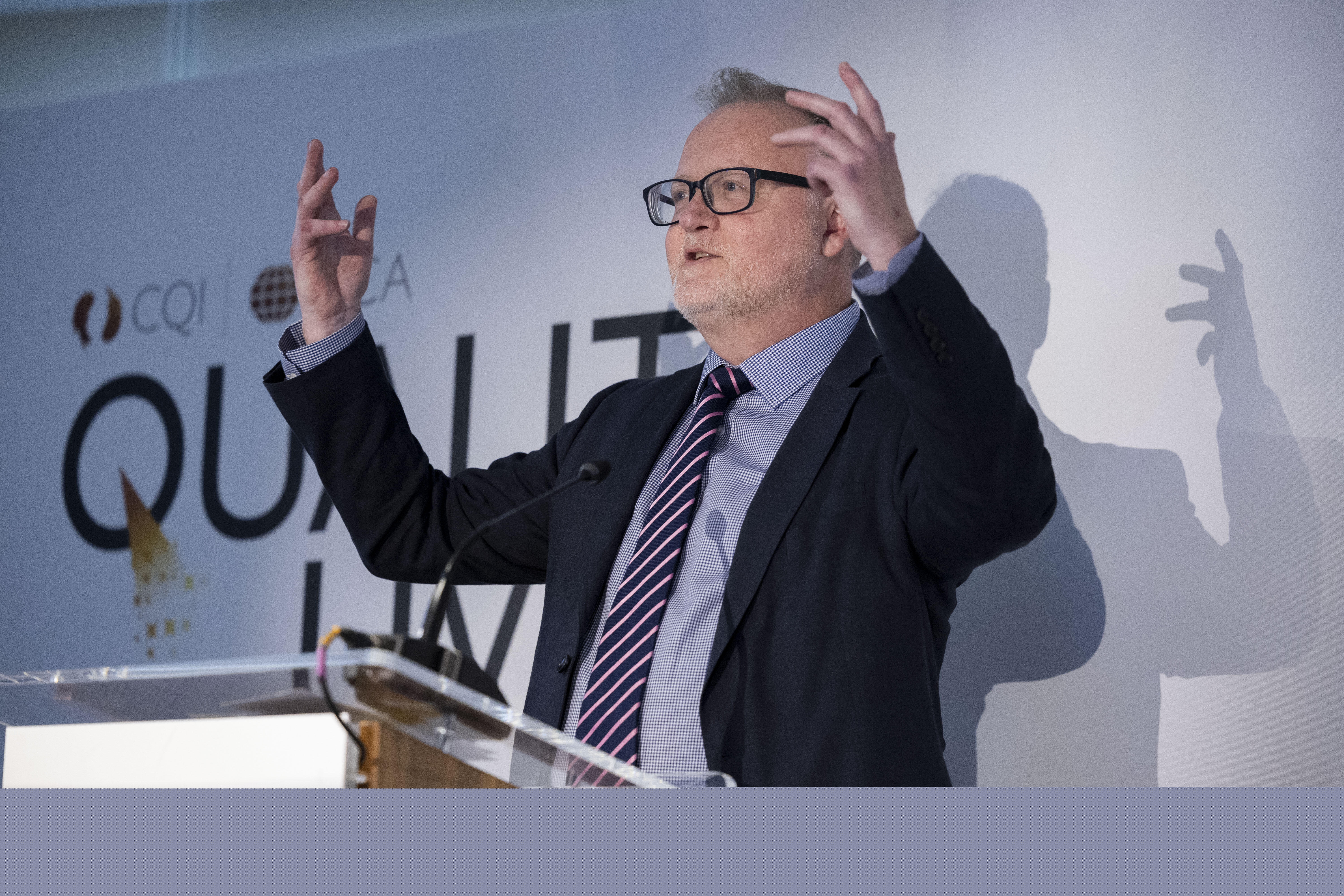 A man stands before a lectern gesturing in a celebratory way with both hands raised